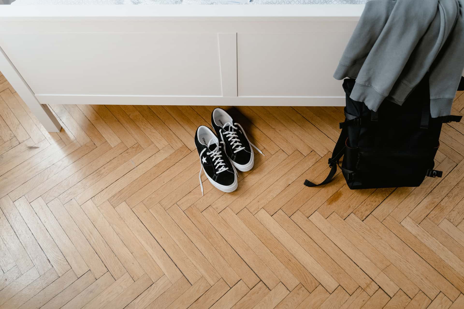 A travel backpack and shoes laid out on a wooden floor before a trip